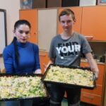 Nauczyciel i uczeń trzyma w rękach blachę z pizzą.