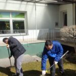 Dwóch chłopców grabi liście przed budynkiem.