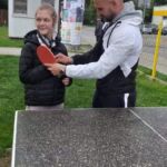 Nauczyciel uczy uczennicą grać w tenis stołowy.